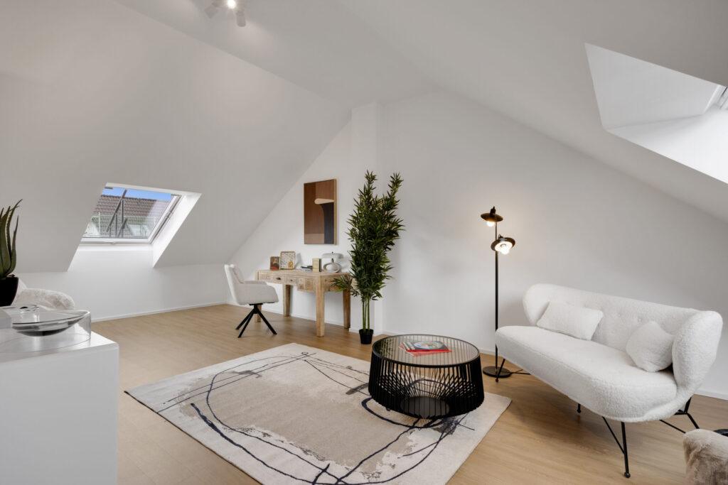 Modernes Dachgeschoss-Wohnzimmer im MoVida Haus mit Schrägdach, gemütlicher Sitzecke und Homeoffice-Bereich zur Miete