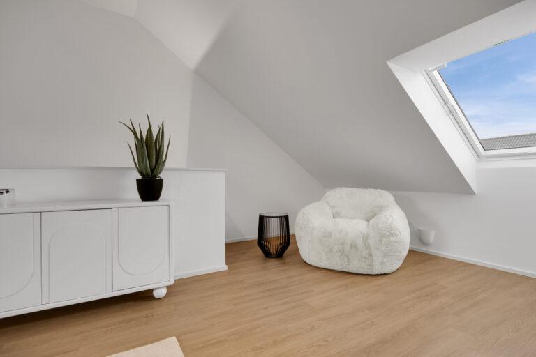 Gemütliche Dachgeschosslounge mit weichem weißen Sessel, modernem Beistelltisch, Sideboard und großem Dachfenster für helles Wohnambiente