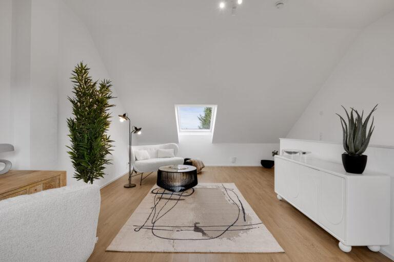 Modernes, helles Dachgeschosszimmer mit gemütlichem Sessel, Designer-Teppich, schwarzem Couchtisch, dekorativen Pflanzen und Dachfenster mit Ausblick