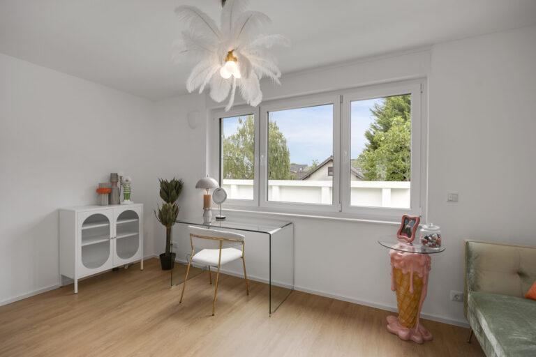 Modernes helles Schlafzimmer mit großem Fenster, Glas-Schreibtisch, Designerstuhl und originellem Beistelltisch in Eiscreme-Optik
