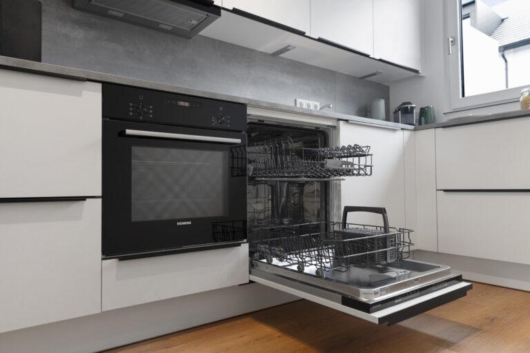 Detailansicht einer modernen Einbauküche mit Backofen und geöffnetem Geschirrspüler in einer Movida-Immobilie zur Miete
