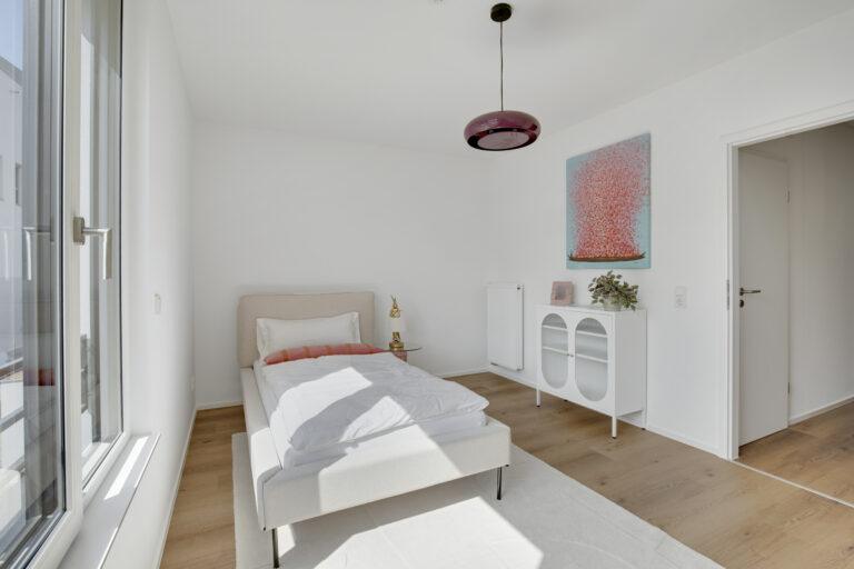 Helles Kinderzimmer mit Einzelbett, großem Fenster und moderner Einrichtung in einer Movida-Immobilie zur Miete