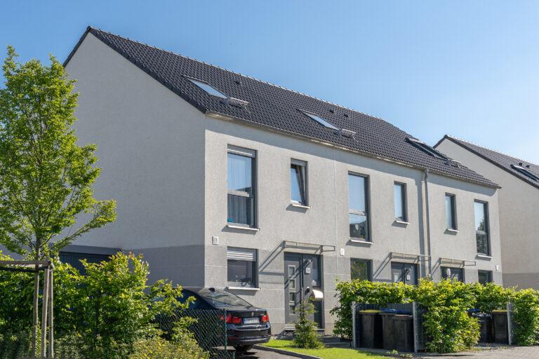 Modernes Movida Neubau-Reihenhaus mit grauer Fassade, großen Fenstern und Satteldach in ruhiger Wohnsiedlung.
