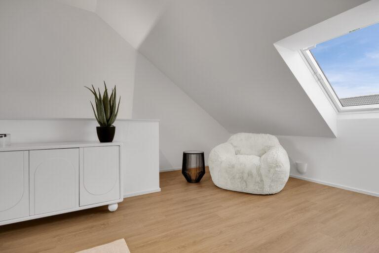 Gemütliche Dachgeschosslounge mit weichem weißem Sessel, modernem Beistelltisch, Sideboard und großem Dachfenster für helles Wohnambiente