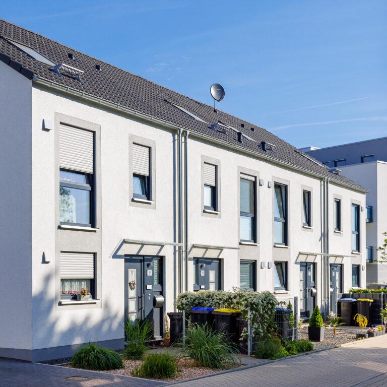 Modernes Movida Neubau-Reihenhaus mit weißer Fassade, großen Fenstern und Satteldach in gepflegter Wohnsiedlung