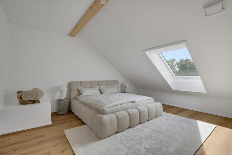Helles Schlafzimmer im Dachgeschoss mit großem Bett, Dachschräge und Fenster in einer Movida-Immobilie zur Miete.
