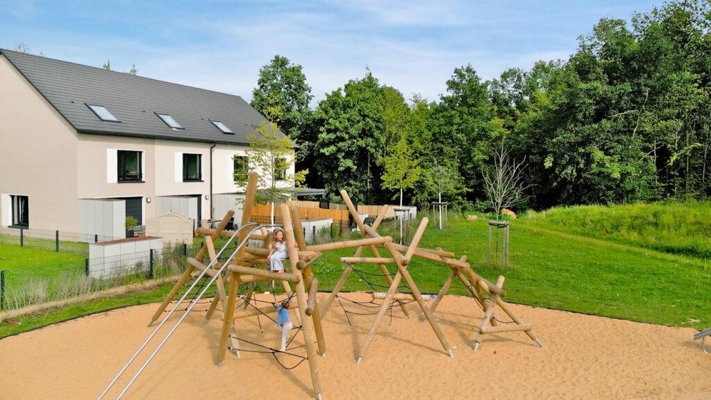 Moderner Spielplatz mit Holz - Klettergerüst vor einer Neubau - Wohnanlage im Grünen