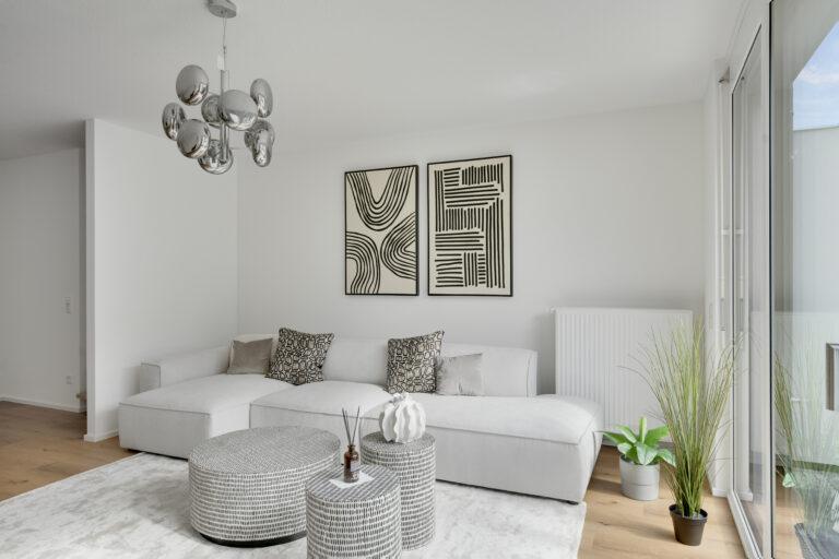 Wohnzimmer mit hellem Sofa, modernen Couchtischen und dekorativer Wandgestaltung in einer Movida-Immobilie zur Miete.