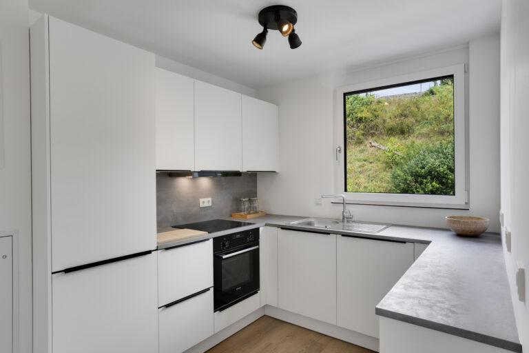 Moderne weiße Einbauküche im MoVida Haus mit Induktionskochfeld, Backofen und großem Fenster