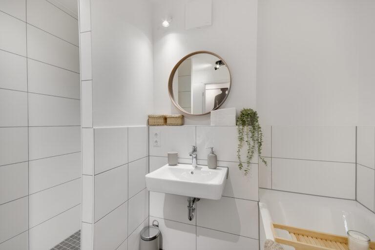 Modernes, helles Badezimmer mit Wand-WC, weißem Waschbecken, Spiegel, begehbarer Dusche und dekorativen Elementen für ein stilvolles Ambiente