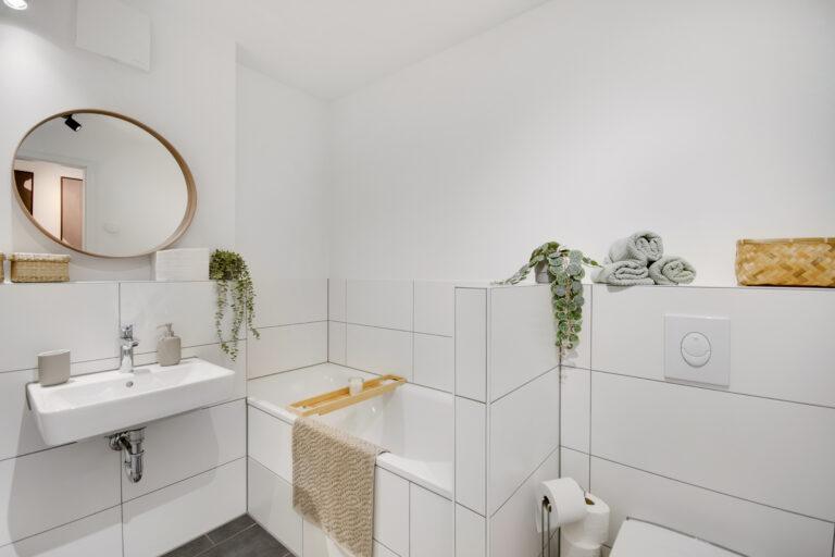 Modernes Movida Badezimmer mit Badewanne, Waschbecken, WC und kleinem Fenster, dekoriert mit Pflanzen