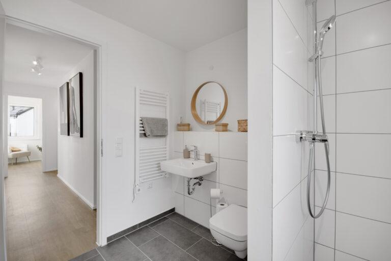 Modernes Badezimmer im Reihenhaus mit Dusche, Wand-WC, Waschbecken und hellen Fliesen.