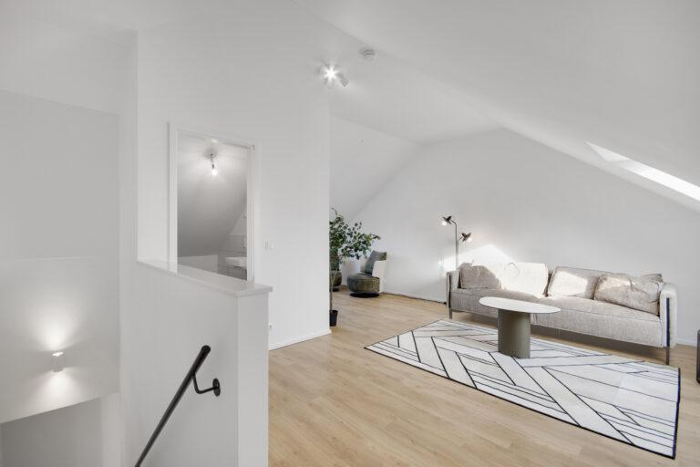 Modernes Wohnzimmer im Dachgeschoss eines Reihenhauses mit Sofa, Holzfußboden und viel Tageslicht.