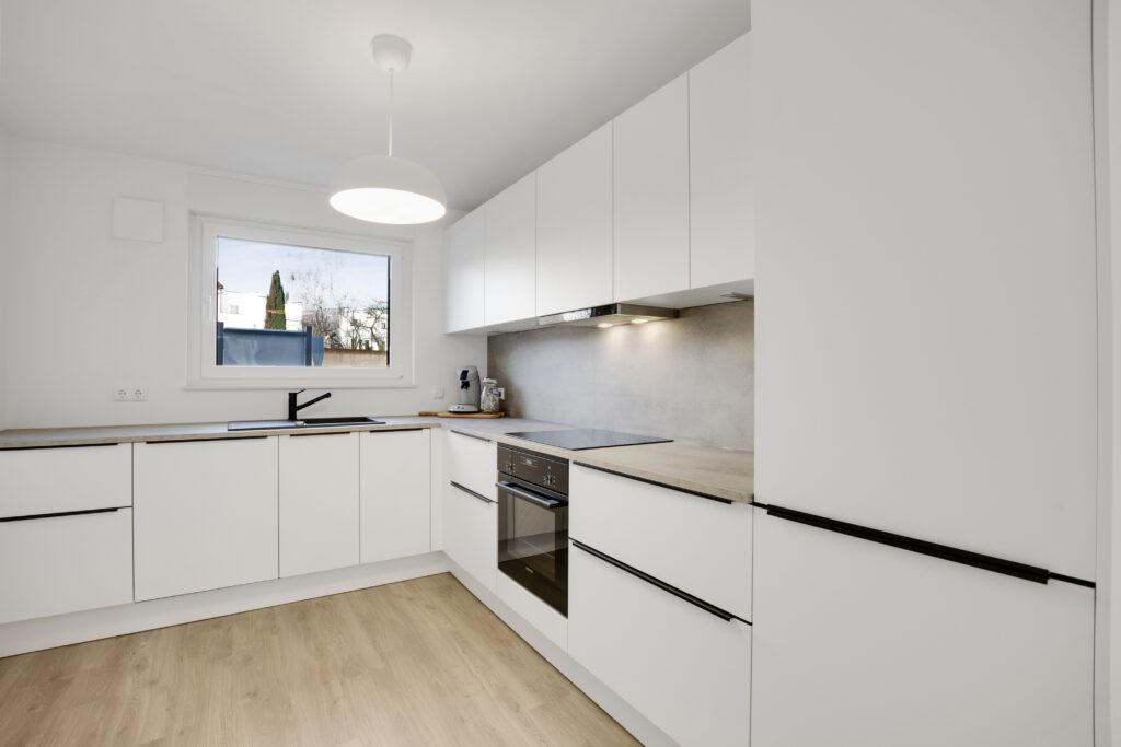 Moderne weiße Einbauküche in L-Form mit Einbaugeräten, heller Arbeitsplatte und Holzfußboden in einem Reihenhaus.