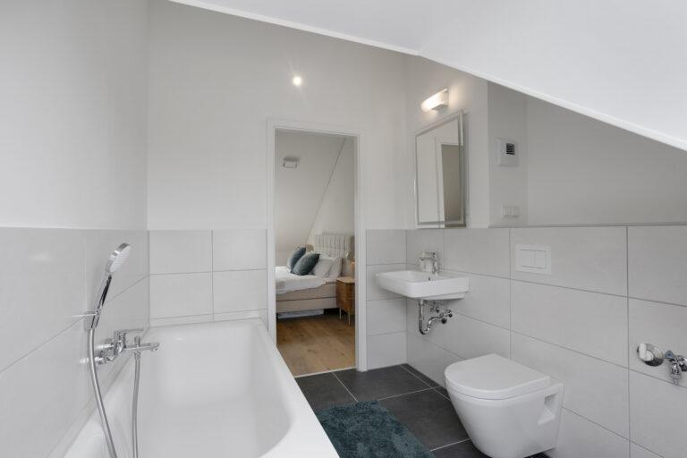 Modernes Movida Badezimmer mit Badewanne, Waschbecken, WC und Blick ins Schlafzimmer