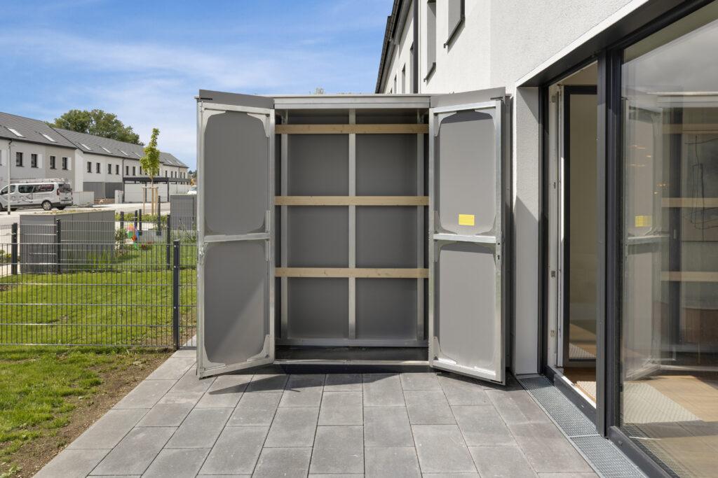 Movida Neubau Außenabstellraum auf der Terrasse mit geöffneten Türen und Blick auf Wohnsiedlung