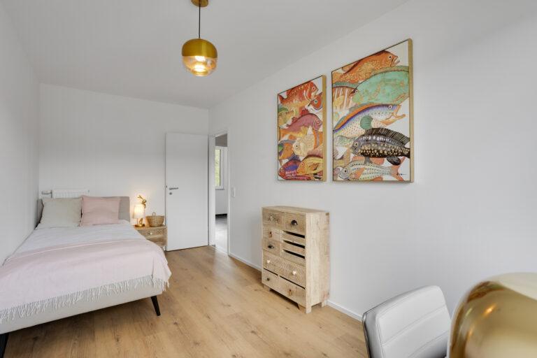 Movida Neubau Schlafzimmer mit Einzelbett, Holzboden, Kommode und bunter Wandkunst